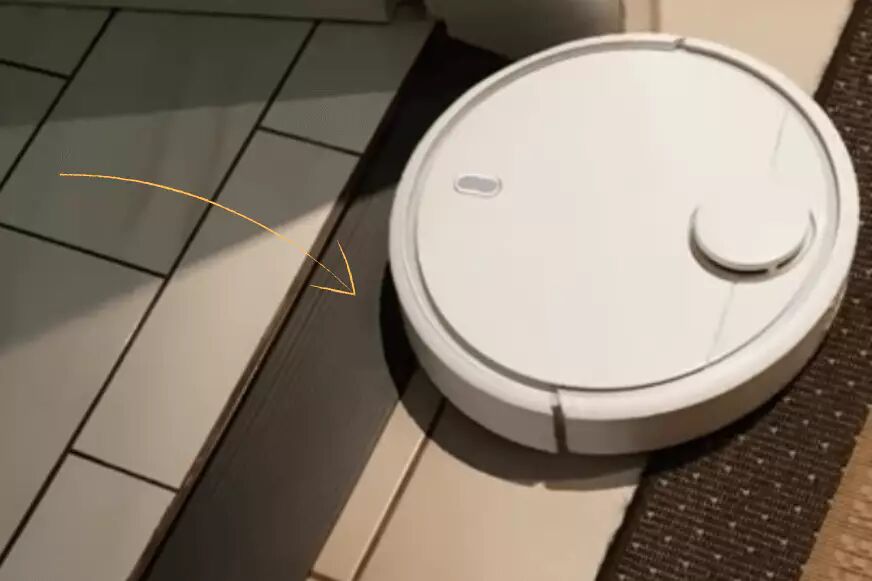 A robot vacuum cleaner crosses a doorstep with the aid of a doorstep ramp.